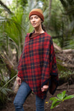 Woman wearing a red plaid poncho and brown beanie standing in a forest